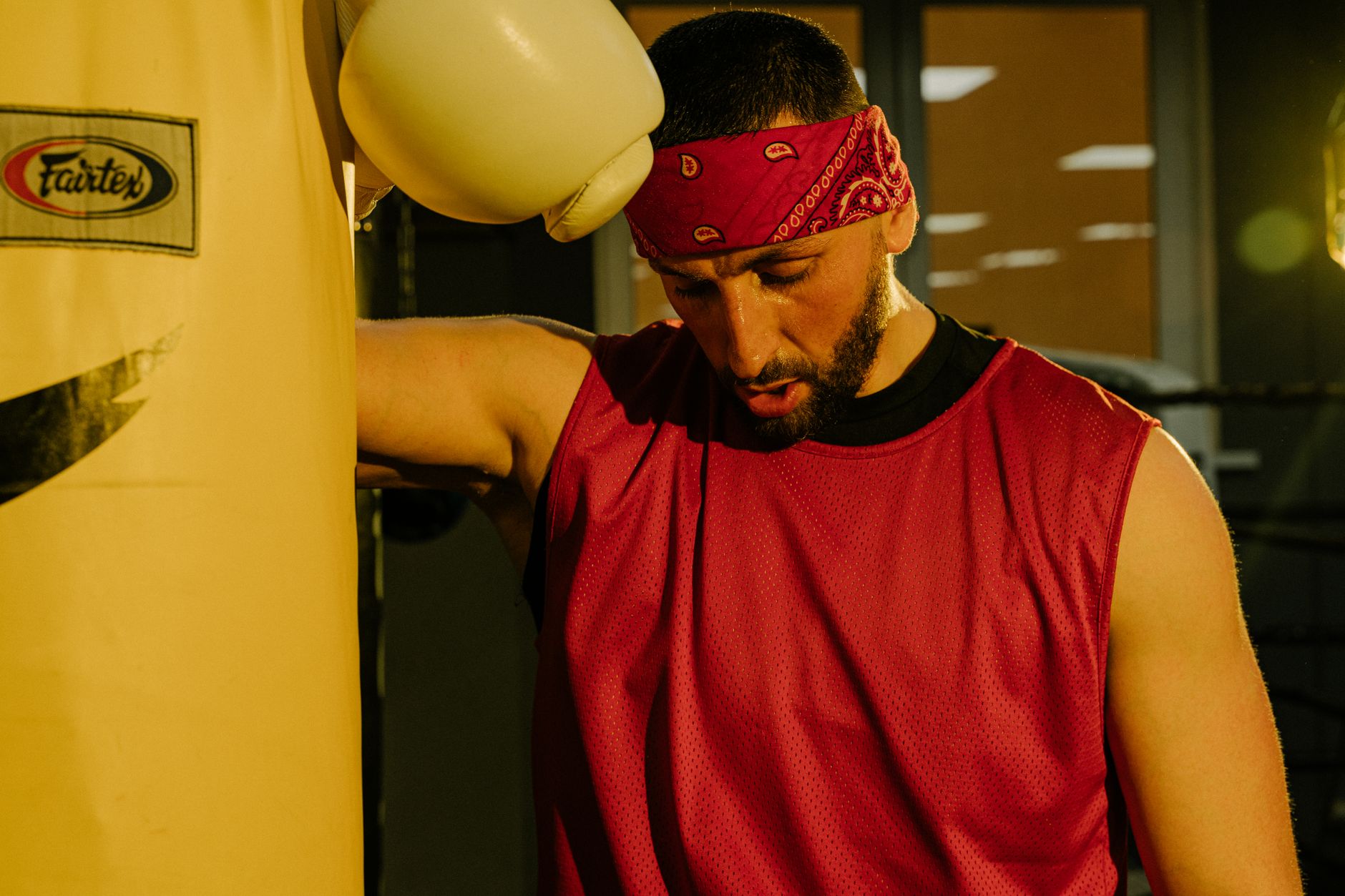 Cardio of krachttraining afvallen: Vastberaden bokser met rode bandana leunt tegen een bokszak in een boksgymnasium