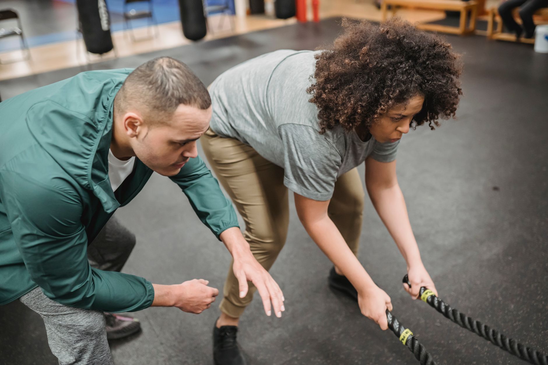 Jonge mannelijke trainer in sportkleding helpt vrouw met overgewicht met battle ropes in moderne sportschool